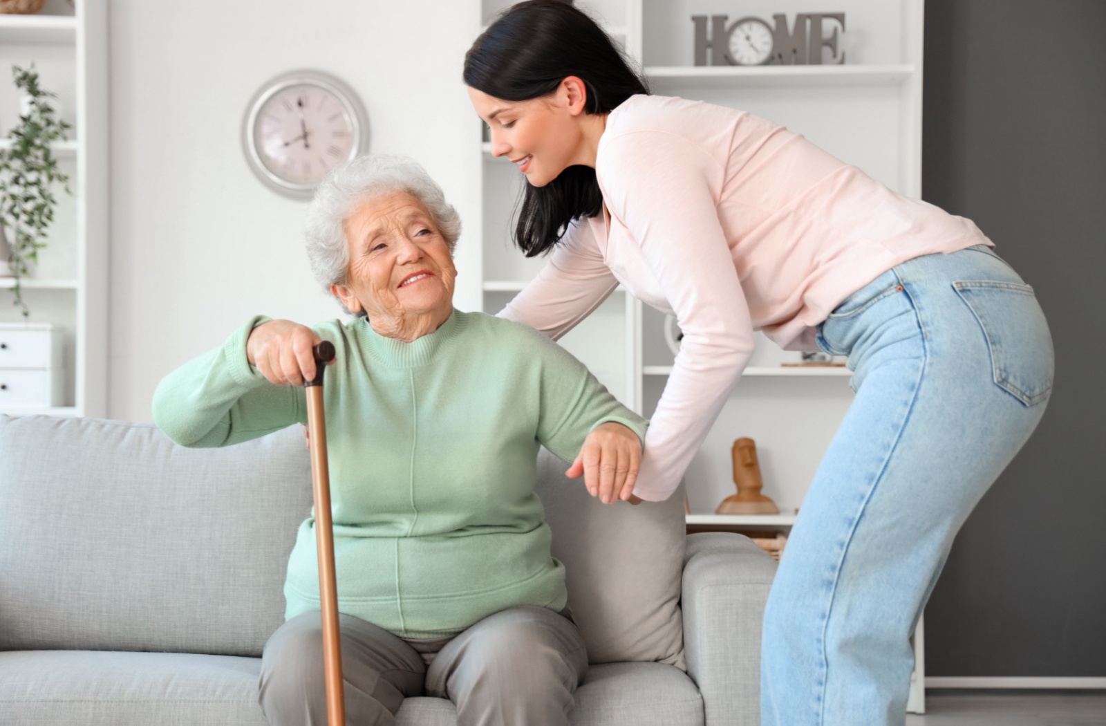 A older adult woman with a cane standing with a help of her daughter.