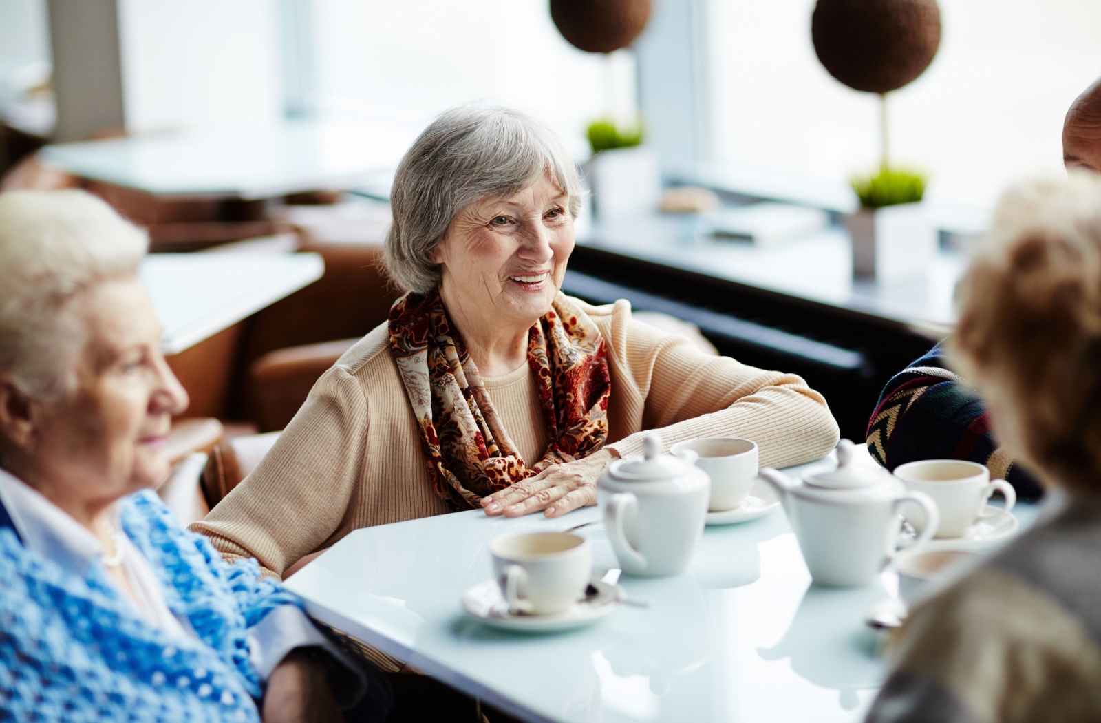 Group of four older people sitting at a table and smiling with cups of tea on the table.