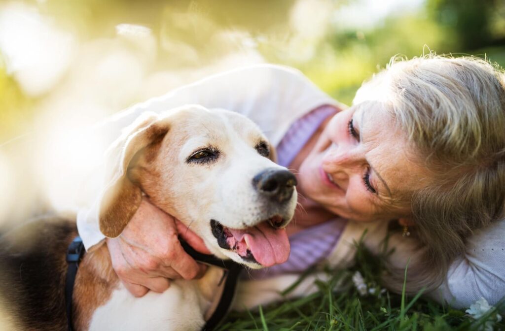 Older adult lying on the grass, smiling and hugging a happy dog.