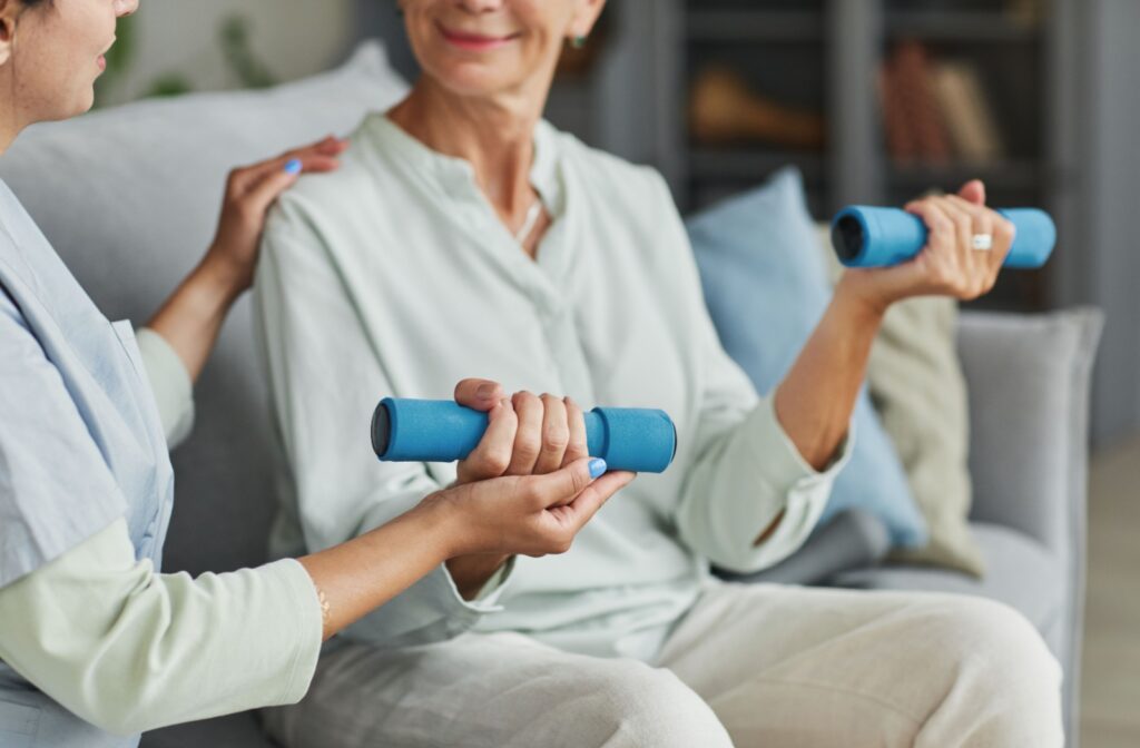 A caregiver helps an assisted living resident lift small weights.