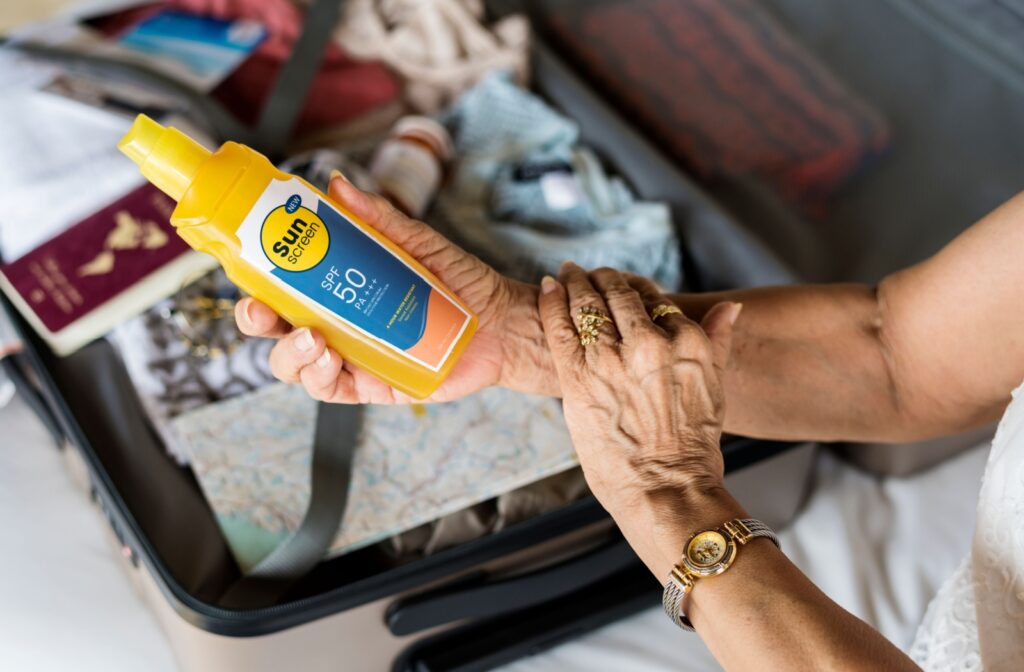 A close-up image of an older adult holding a yellow bottle of sunscreen as they get ready for the summer sun.