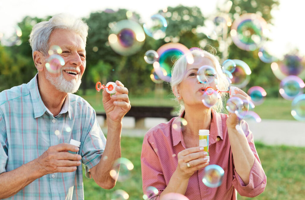 An older couple laughing outside during summer while blowing bubbles together in a park.