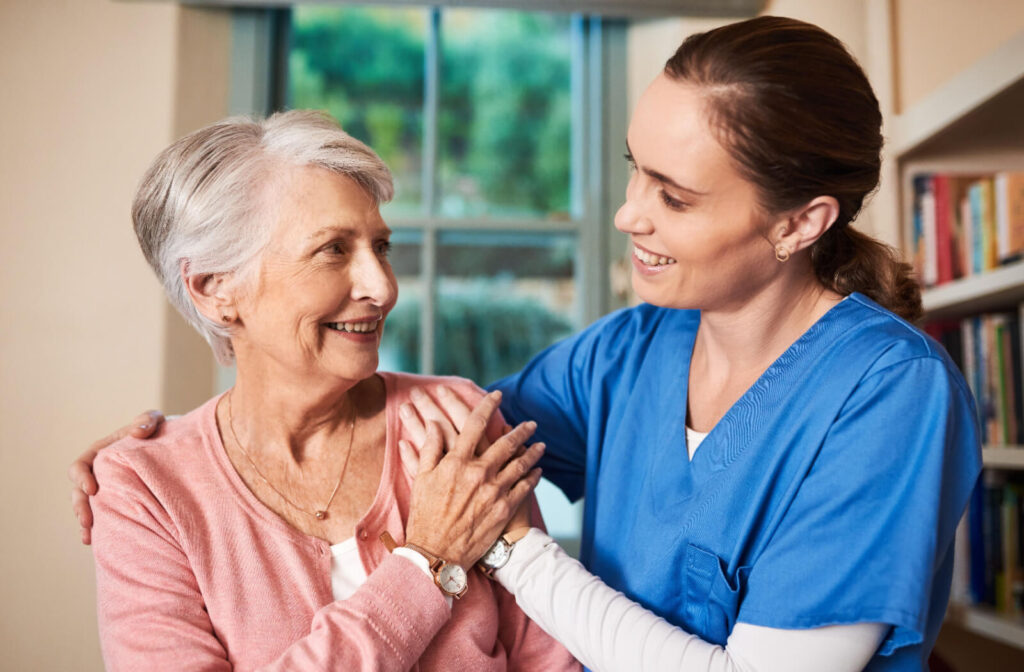 A caregiver hugging a resident in assisted living while they smile at one another.