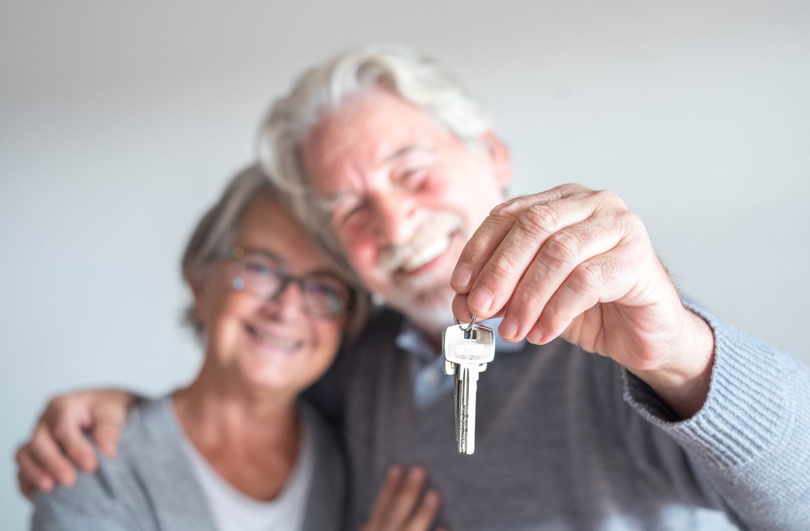 An older couple smiling while holding up the key to their new home in assisted living.