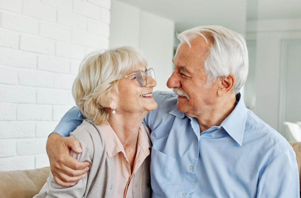 An older couple lovingly looking at each other while sitting on their couch in assisted living.