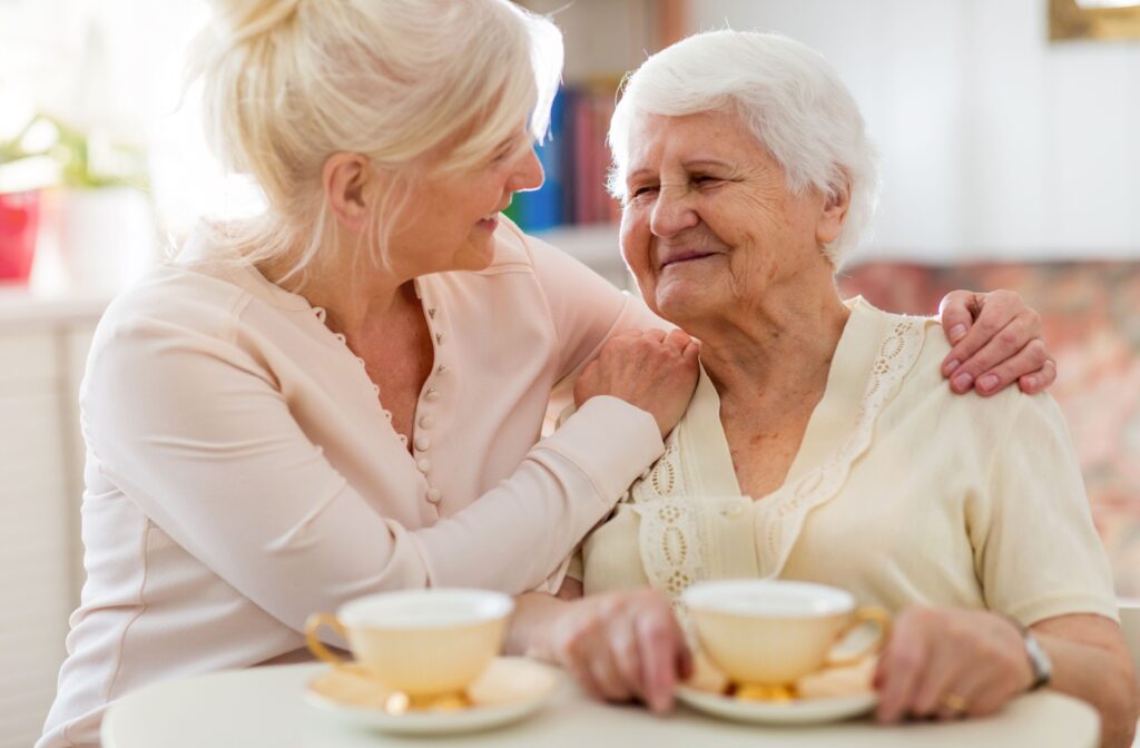 An older woman sitting at the table having tea with her older daughter.