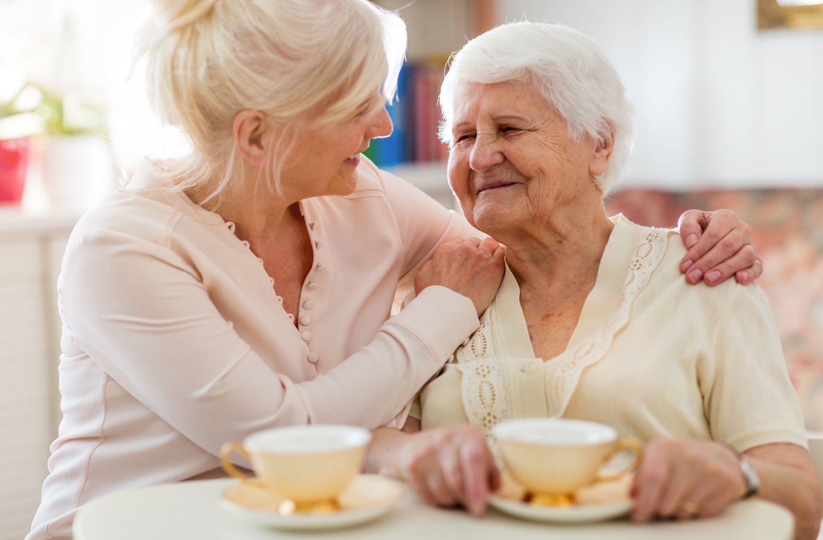 An older woman sitting at the table having tea with her older daughter.
