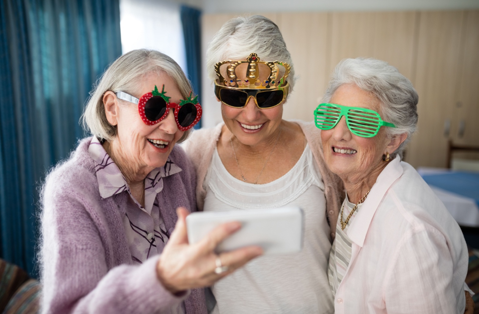 Three senior friends wearing novelty glasses take a picture together, highlighting their friendship in assisted living