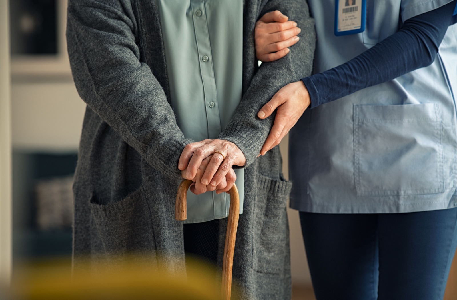 A caregiver holds the arm of an older adult with a cane while walking together through an assisted living community