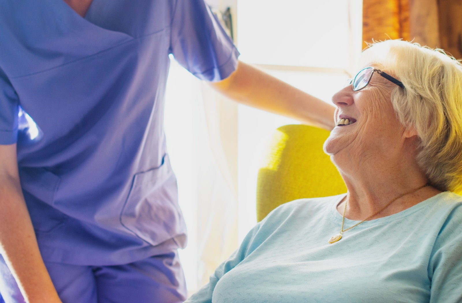 a caregiver checking on a senior sitting on an armchair